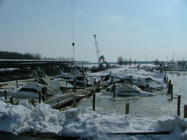 Boats covered in snow and ice at a marina with cranes in the background