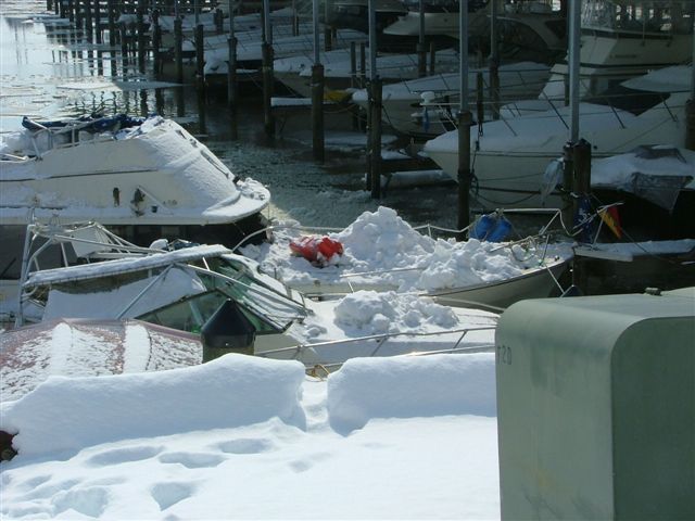 Boats covered in snow at a marina with ice on the water