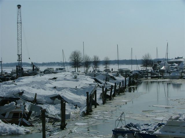 Marina in winter with boats covered in snow and ice, a large crane visible