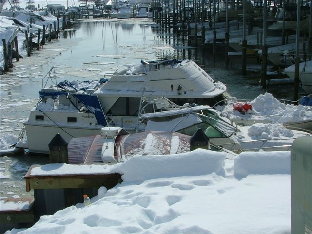 Boats in a frozen marina covered in snow, with some debris