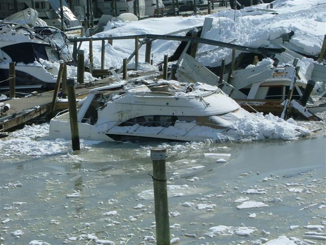 Boats wrecked in a marina with snow and ice covering them and the water