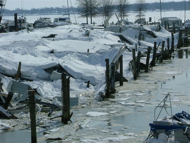 Boats and docks heavily damaged and covered in snow and ice at a marina