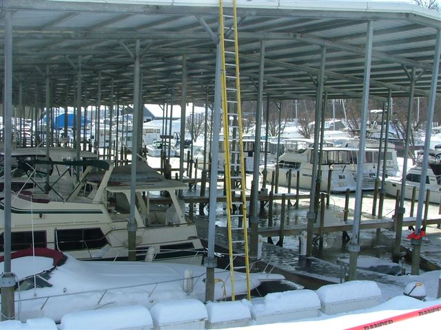 Boats covered in snow docked under a metal canopy at a marina
