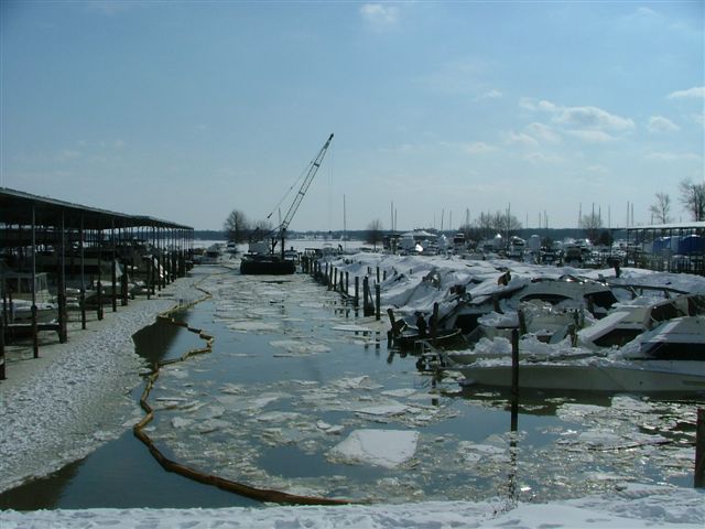 Marina docks covered in snow with ice floes in the water and a crane visible