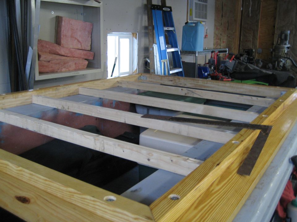 Wooden frame with metal square and ruler on top of a white surface, with insulation and a ladder in the background