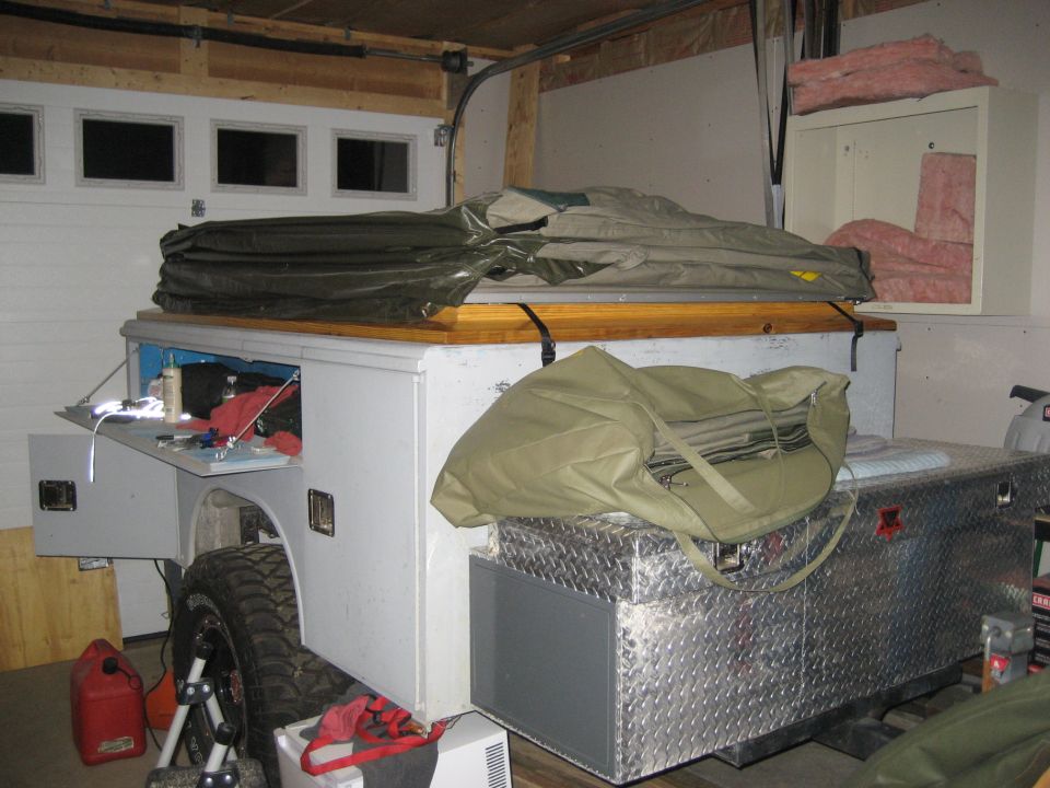 Truck bed camper shell with storage compartments and a tent on top, parked in a garage