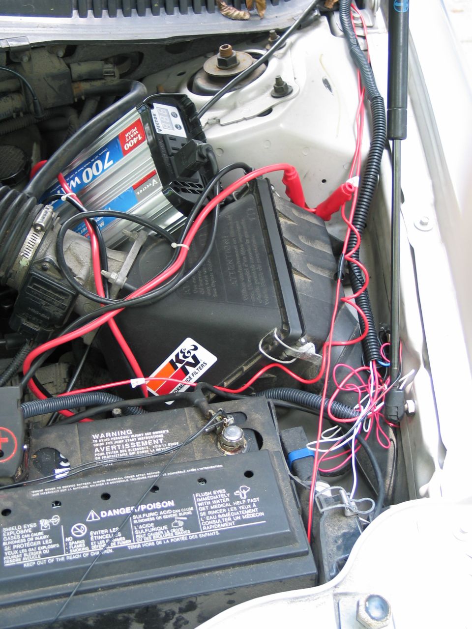 Engine-bay corner showing a battery, Motorcraft 700 battery box and tangled red and black wiring