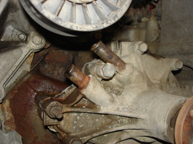 Close-up of a corroded engine water pump with two pipes and a pulley visible