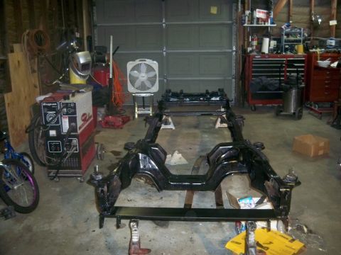 1985 Ford Bronco - A vehicle frame is elevated on jack stands in a garage, awaiting further restoration work.