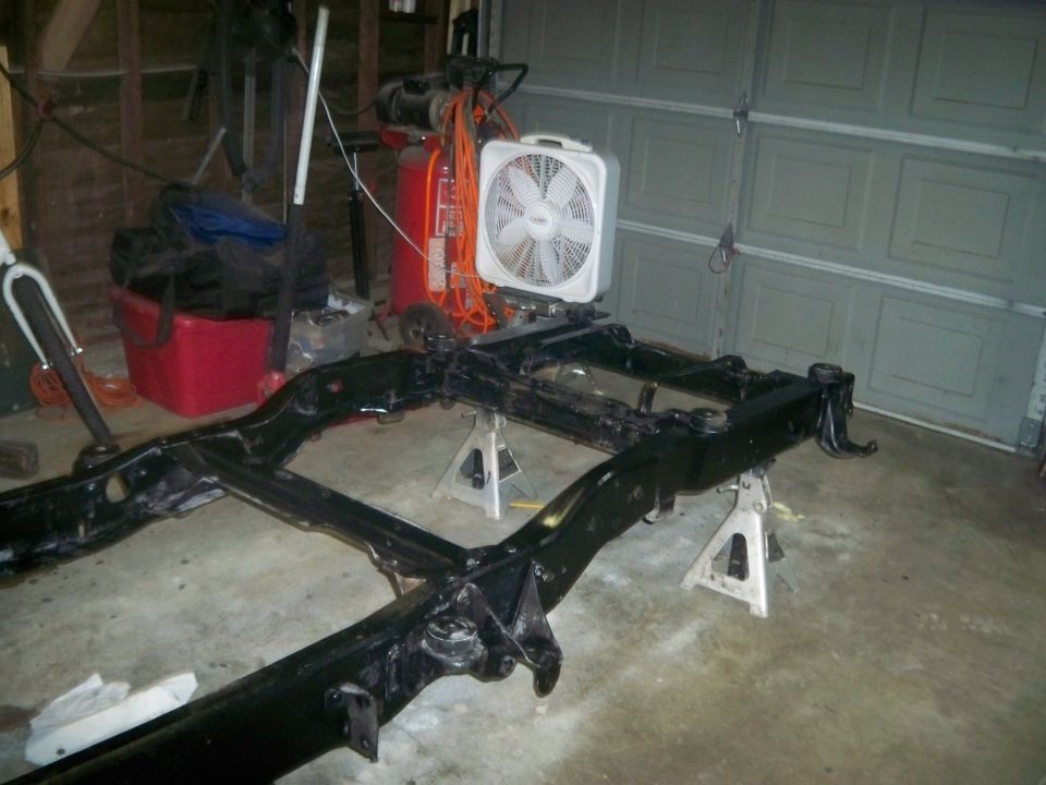 Black vehicle frame on jack stands in a garage