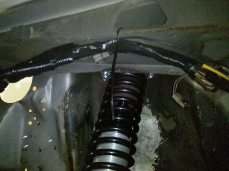 Close-up of a black coil suspension spring and bundled black wiring harness in a vehicle's undercarriage