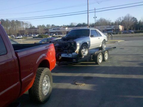 1986 Ford Mustang - Silver 1986 Ford Mustang being transported on a trailer, with its front end disassembled.