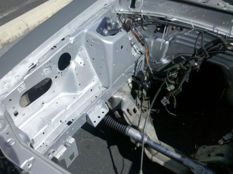 1986 Ford Mustang - Freshly painted silver engine bay and front inner structure of a stripped unibody car photographed from above, with bare shock towers, dril…