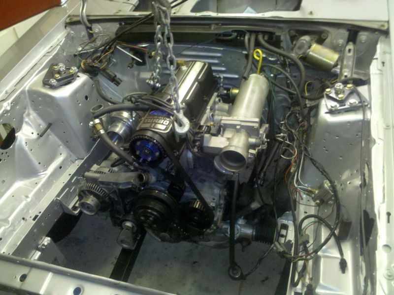 Turbo four-cylinder engine being set into a bare painted engine bay by a chain