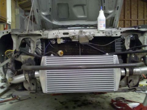 1986 Ford Mustang - Front-end view of a stripped vehicle in a garage/workshop with a large silver aluminum front-mount intercooler installed behind the front o…