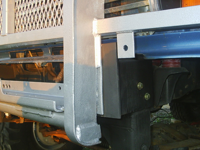 Close-up of silver brush guard mounting bracket bolted to the front of a blue truck