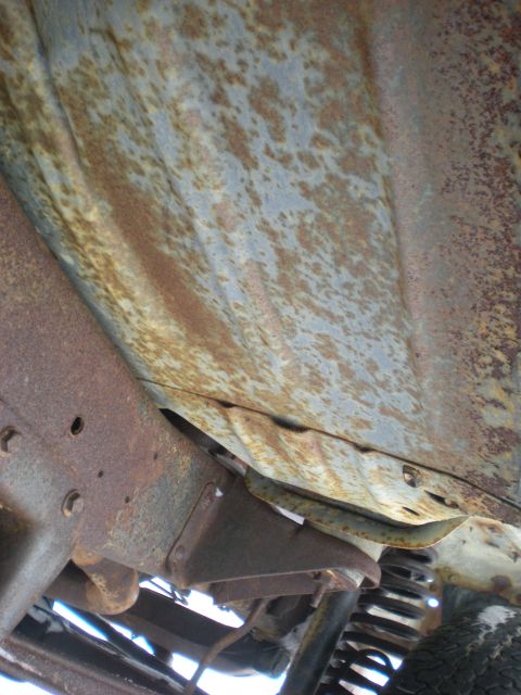 1978 Ford Bronco - The undercarriage of a vehicle shows significant rust and wear on its frame and body panels.
