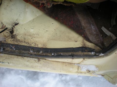 1978 Ford Bronco - Close-up of a dirty car interior panel and rubber seal, with visible snow on the exterior.