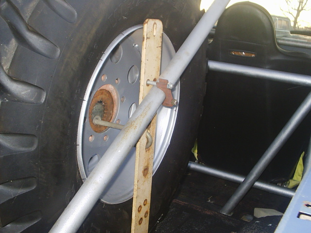 Big off-road spare tire on a steel wheel held by a homemade wood-and-tube rack inside a vehicle