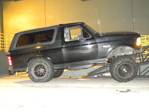 1995 Ford Bronco - A black Ford Bronco is positioned on a metal ramp, showing its lifted suspension and large tires.