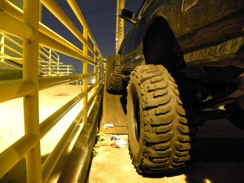 1995 Ford Bronco - A vehicle with large, aggressive tires is positioned next to a yellow barrier, with a dark sky overhead.