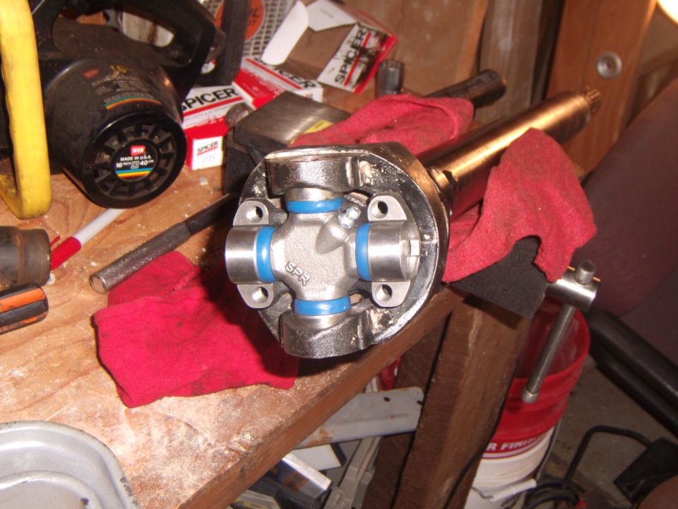 Universal joint with blue seals on a workbench, with tools and parts in the background