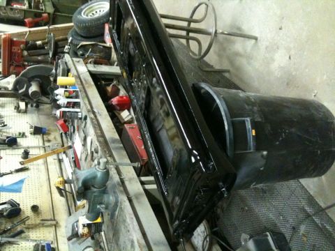 1993 Ford Bronco - A black vehicle door and fender are laid out on a workbench in a garage, surrounded by tools and spare tires.