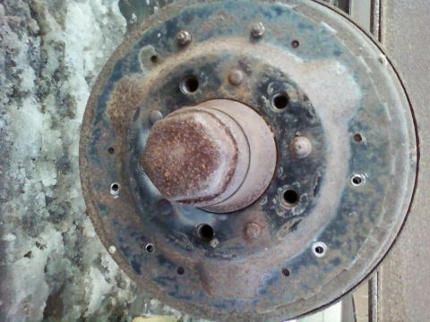 1985 Ford F-150 - Close-up of a heavily rusted brake drum and hub assembly, showing bolt holes and a central nut.