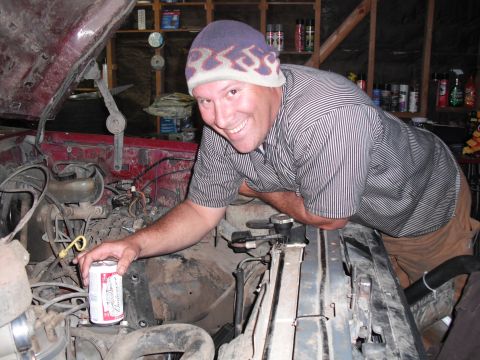 1991 Ford Bronco - Man poses with a can of beer while working on the engine of a red vehicle in a garage.