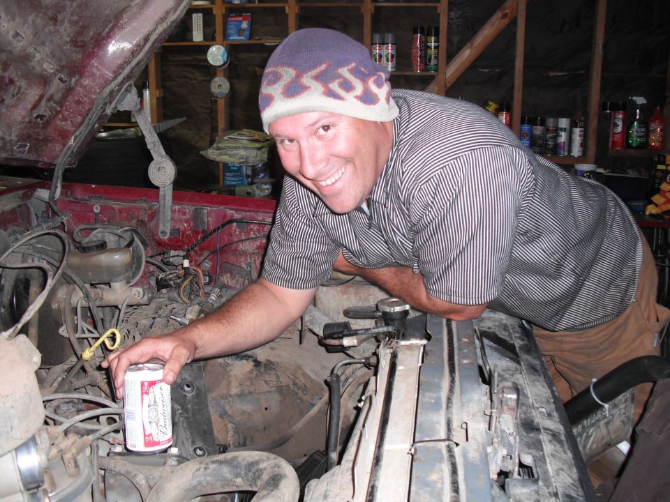 Man with beer can in engine bay, red vehicle