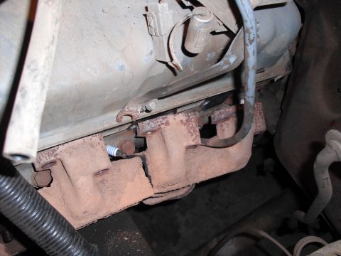 1991 Ford Bronco - This image shows a close-up view of a vehicle's exhaust manifold and a spark plug, indicating engine components.