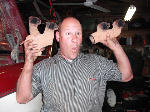 1991 Ford Bronco - Man holds exhaust manifold parts in front of a red vehicle in a garage.