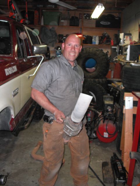 1991 Ford Bronco - A man holds a custom exhaust pipe in a garage, with a red and white truck partially visible.