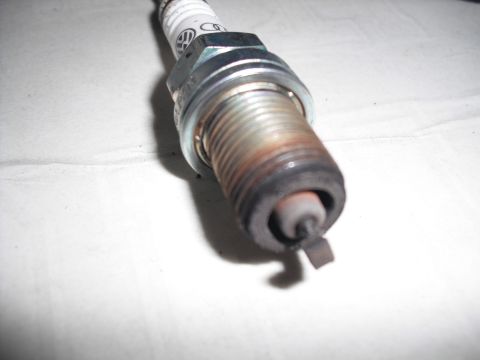 1991 Ford Bronco - Close-up of a used spark plug, showing wear and a Volkswagen logo on the insulator.