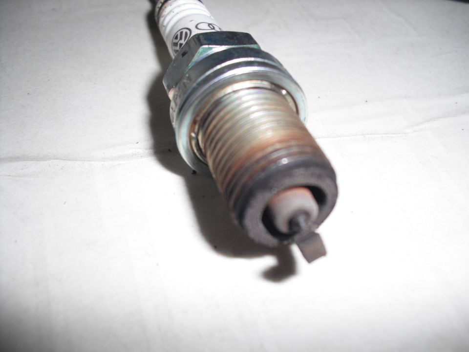 Used spark plug with visible carbon buildup and a VW logo on the ceramic insulator