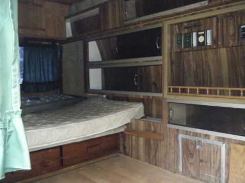 1981 Ford E350 - The interior of a camper van features a bed, wooden cabinets, and a control panel, suggesting a vintage recreational vehicle.
