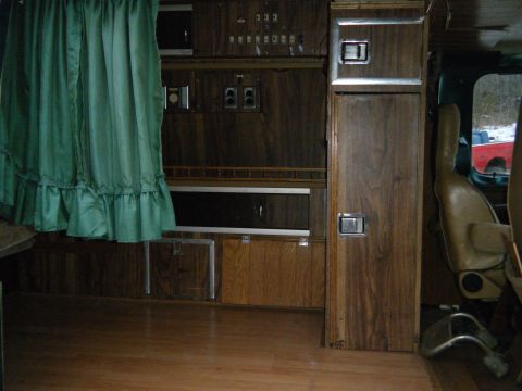 1981 Ford E350 - Interior of a van showing wood paneling, curtains, and a seat; a red truck is visible outside.