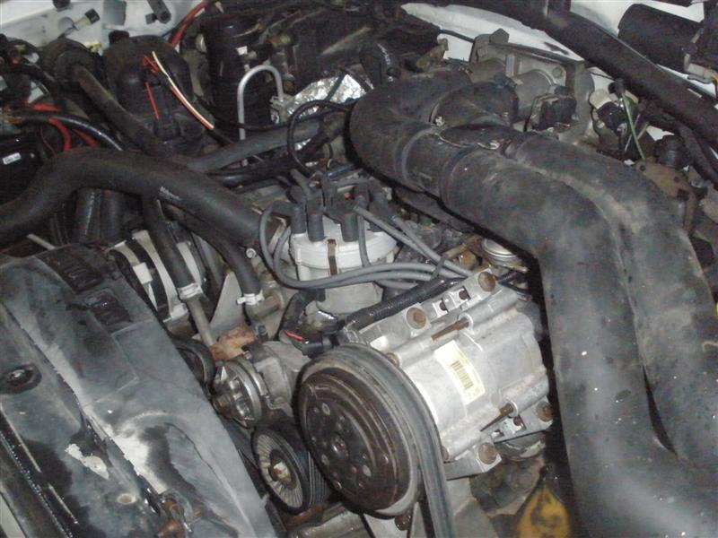 Grimy V8 engine bay with A/C compressor, distributor cap and black intake duct