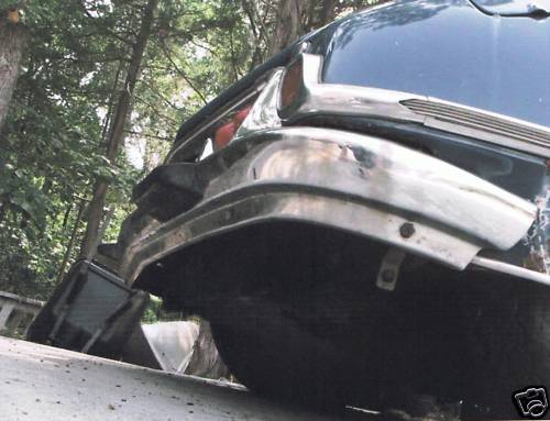 Low-angle rear view of a dark car's chrome bumper and taillight outdoors
