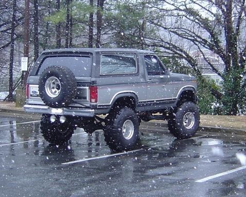 1986 Ford Bronco - A lifted Ford Bronco sits in a parking lot during a snowfall.