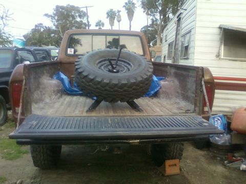 1976 Ford F-250 - Rear view of a brown pickup truck with a spare tire in the bed, parked next to a trailer.