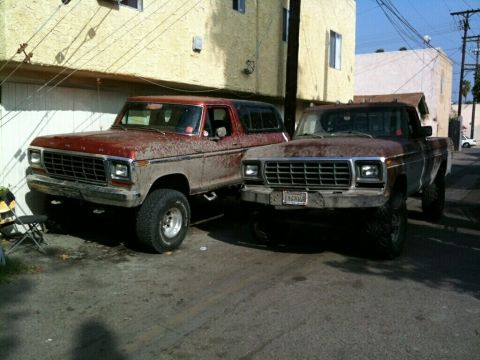 1976 Ford F-250 - Two older Ford trucks, a Bronco and a pickup, are parked in an alleyway.
