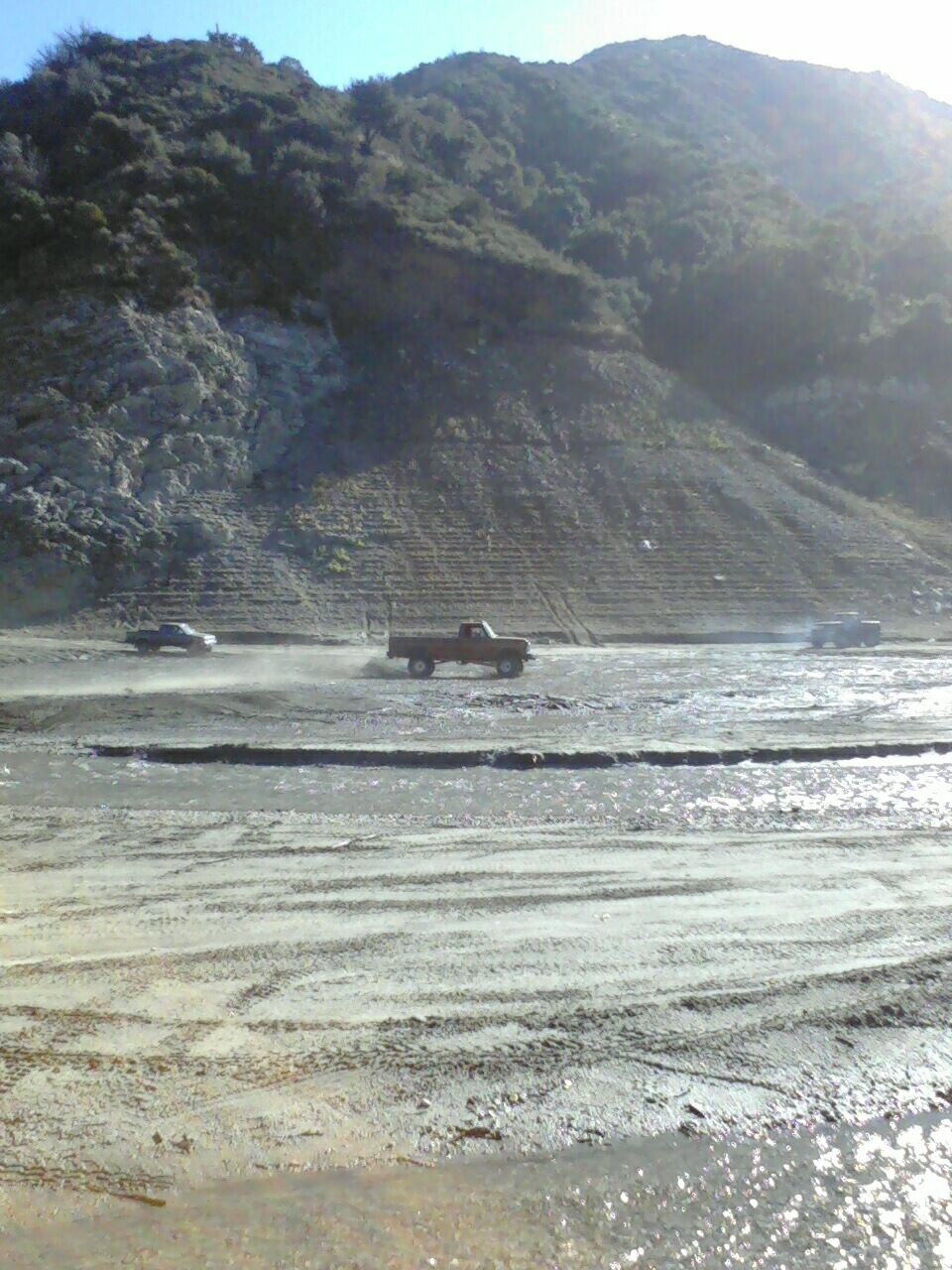 Brown 1973 Ford F-250 driving on a muddy road with a hill in the background