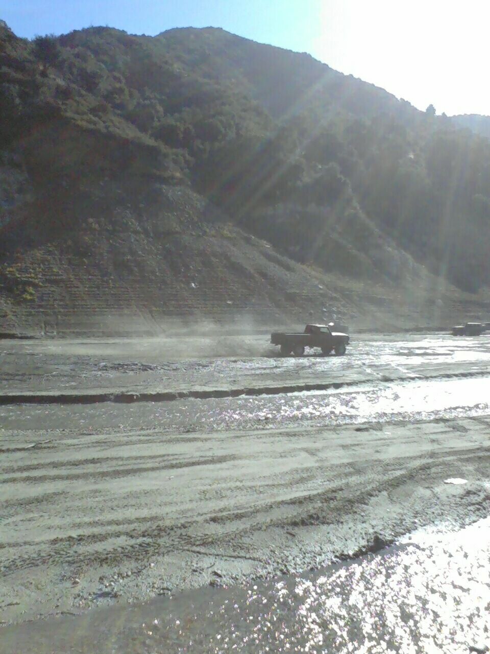 Side view of a 1976 Ford F-250 driving through a dusty, wet terrain with another truck in the background