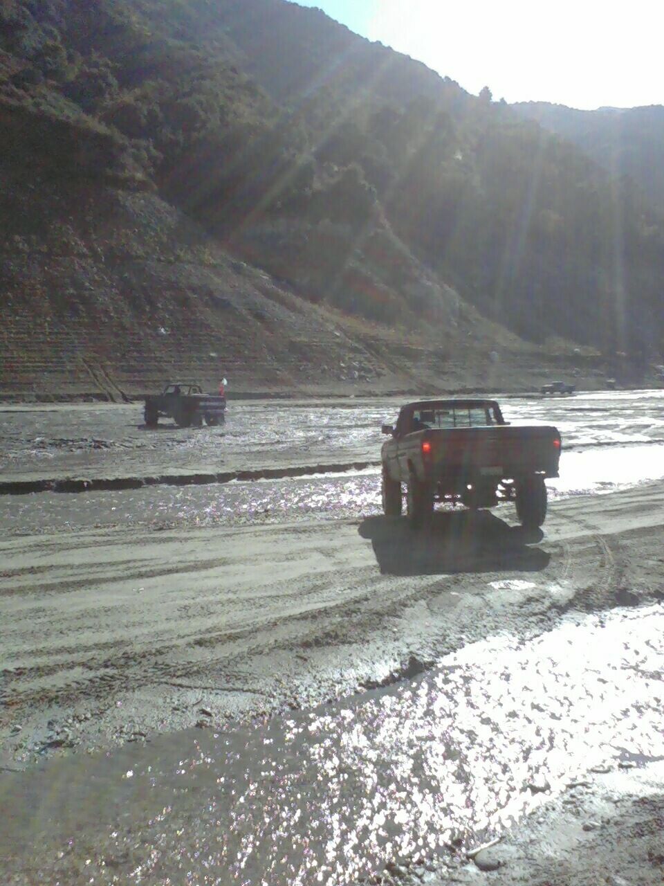 1976 Ford F-250 driving through mud with another truck in the background