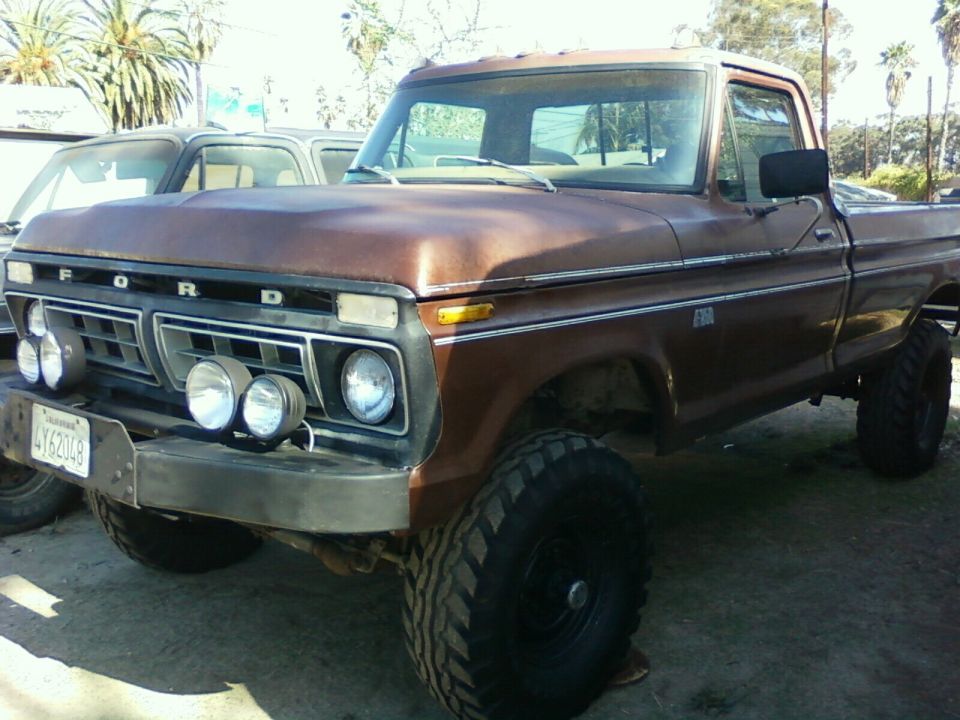 Brown 1973 Ford F-250 pickup truck with aftermarket lights and large tires, parked next to another vehicle