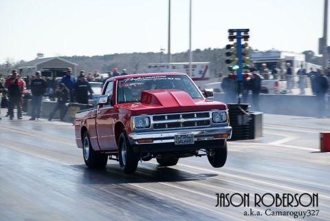1992 Ford Mustang - A red pickup truck launches off the starting line at a drag race, its front wheels airborne.