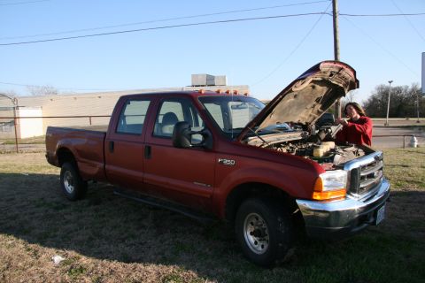 1993 Ford Bronco - A person works on the engine of a red Ford F-350 pickup truck parked outdoors.