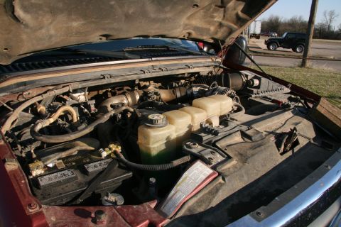 1993 Ford Bronco - The engine bay of a vehicle is shown with the hood open. A black SUV is parked in the background.