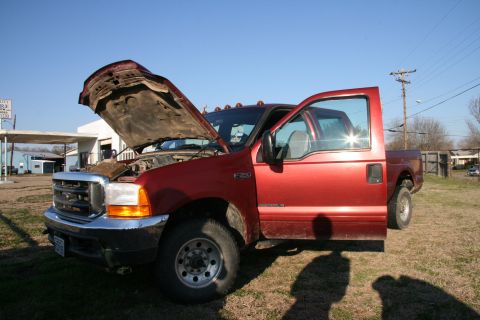 1993 Ford Bronco - Red Ford F-350 truck with hood and driver door open, parked in a grassy area near a building.